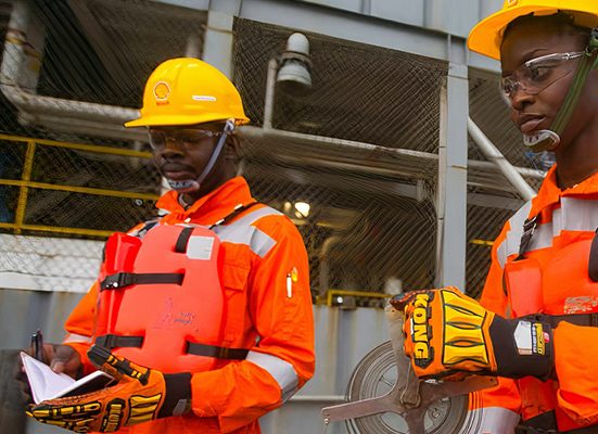 Two Westshore Oil & Gas technicians in high-visibility coveralls and life vests recording production readings on a platform