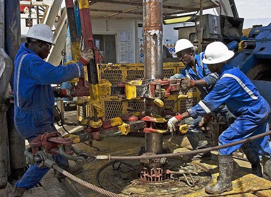 Rig crew in blue coveralls and hard hats operating power tongs on a wellhead during well completion